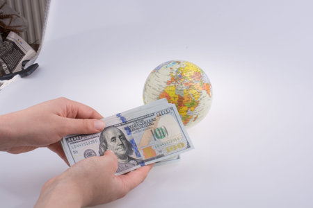 Human hand holding American dollar banknotes by the side of a model globe on white background