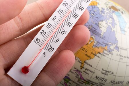 Hand placing a thermometer on a little model globeの写真素材
