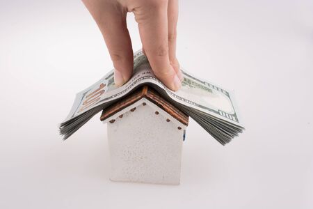 Hand holding American dollar banknotes on the roof of a model house  on white backgroundの写真素材