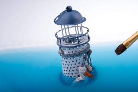 Painting brush and little model lighthouse  placed in blue waterの写真素材