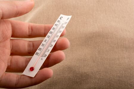 Hand holding a thermometer on a brown color backgroundの写真素材