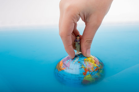 Hand holding a little figurine on the top of the globe in waterの写真素材