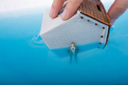 Man figurines in water by the side of  a Little model houseの写真素材