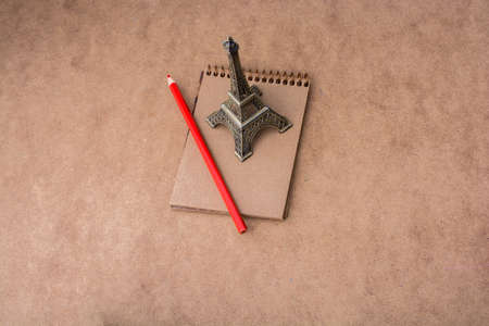 Little model Eiffel Tower, notebook and a pencil on brown backgroundの写真素材