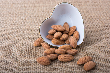 Almonds in a heart shaped plate on canvas background