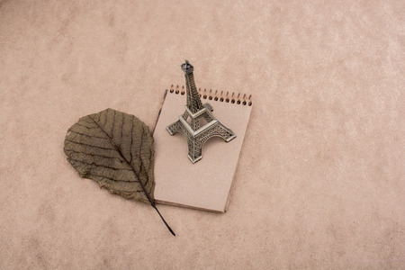 Little model Eiffel Tower, notebook and a dry leaf on brown backgroundの写真素材