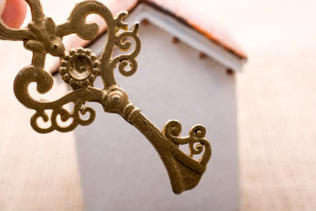 Hand holding a retro key by a model house  on a brown color backgroundの写真素材