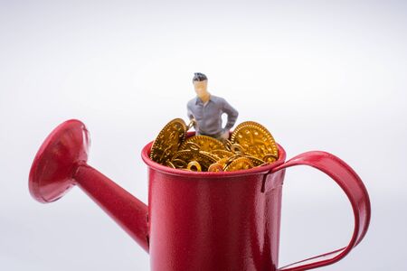 Figurine man standing in a watering can full of fake  gold coinsの写真素材