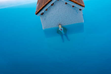Man figurines in water by the side of  a Little model houseの写真素材