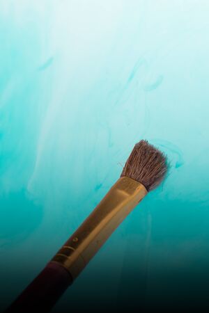 Watercolor paint dissolving in water as painting brush touches waterの写真素材