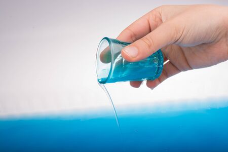 Water pouring down out of blue color glass in handの写真素材