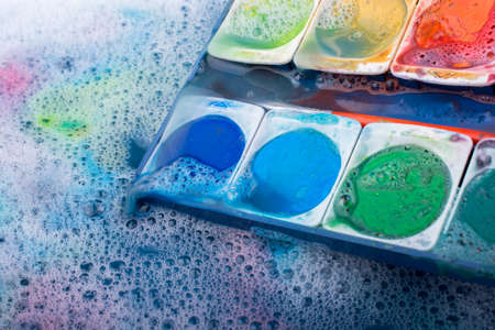 Watercolor paint dissolving in water covered with foamの写真素材