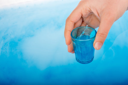 Blue color glass in hand over blue  color water
