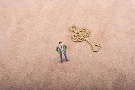 Figurine standing by a retro styled golden color key on a brown backgroundの写真素材