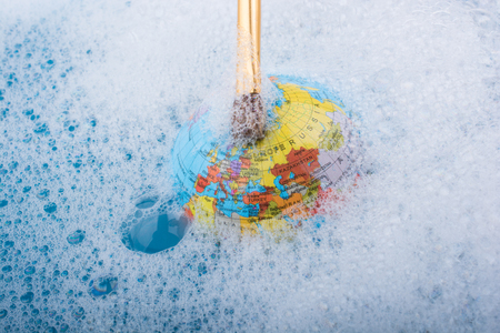 Paint brush placed on the top of globe in a water covered with foamの写真素材