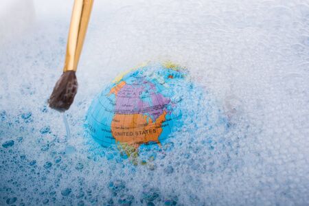 Paint brush placed on the top of globe in a water covered with foamの写真素材