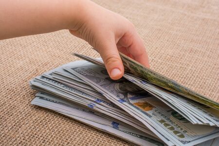 Toddler hand holding banknote bundle of US dollar on a linen canvas backgroundの写真素材