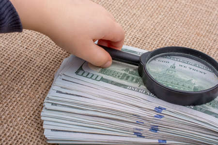 Toddler holding a magnifying glass  over the banknote bundle of US dollarの写真素材