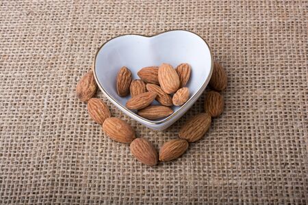 Almonds in a heart shaped plate on canvas backgroundの写真素材