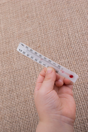 Hand holding a thermometer on a brown color background