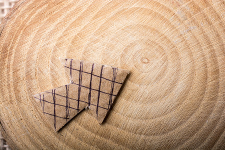 Arrow sign cut out of brown paper on piece of wood