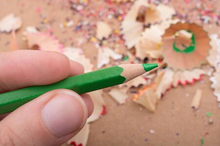 Hand holding Color Pencil over a notebook with pencil shavingsの写真素材