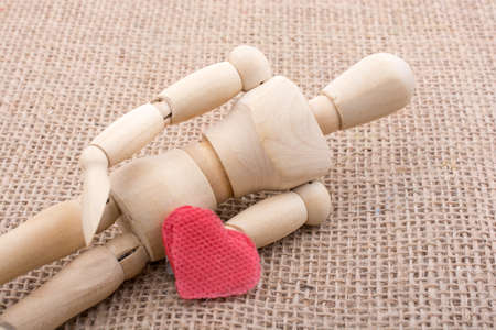 Heart shaped object  in the hand of a wooden man toyの写真素材