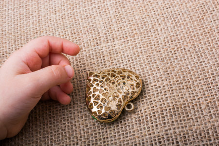 Heart shaped gold color metal object  beside a hand