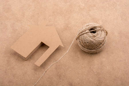 House shape cut out of paper and spool of thread brown backgroundの写真素材