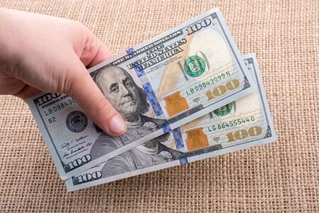 Hand holding banknote bundle of US dollar on a linen canvas backgroundの写真素材