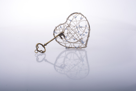 Key and a heart shaped metal cage on whiteの写真素材