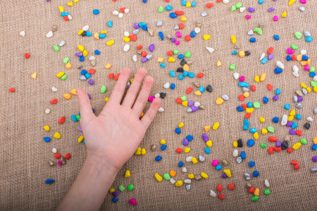Hand placed on colorful pebbles on canvas backgroundの写真素材