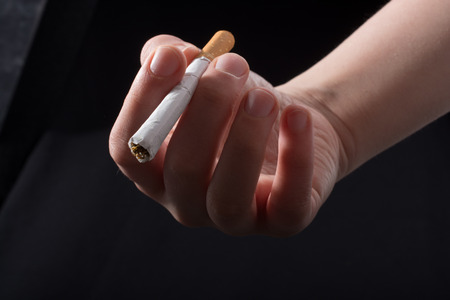 Hand is giving out cigarette on a black backgroundの写真素材