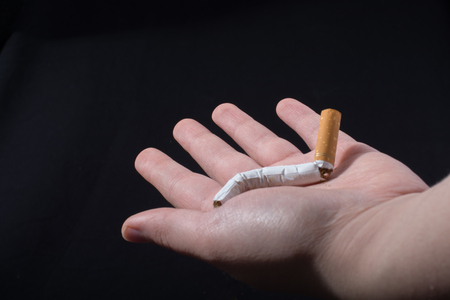 Hand is breaking a cigarette on a black backgroundの写真素材