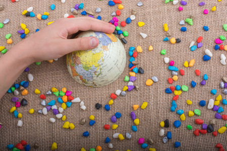 Hand holding globe placed amid colorful pebblesの写真素材