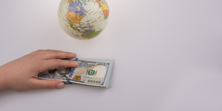 Human hand holding American dollar banknotes by the side of a model globe on white backgroundの写真素材