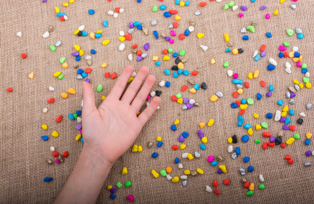 Hand placed on colorful pebbles on canvas backgroundの写真素材