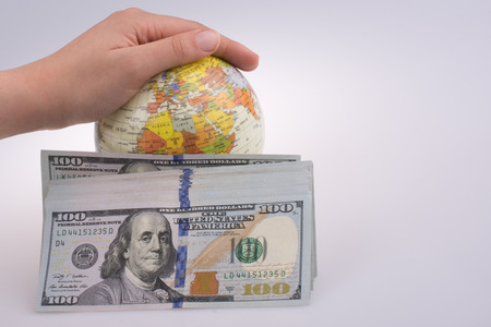 Human hand holding  a model globe by the side of aAmerican dollar banknotes on white backgroundの写真素材