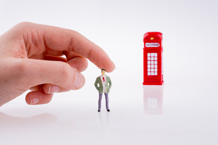 Hand holding a figure near a phone booth on a white backgroundの写真素材