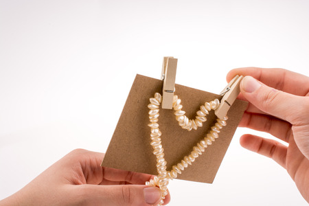 Pearl necklace forms heart shape on paper on white backgroundの写真素材