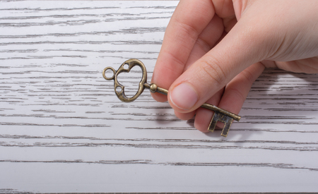 Hand holding a retro styled decorative key on wooden textureの写真素材