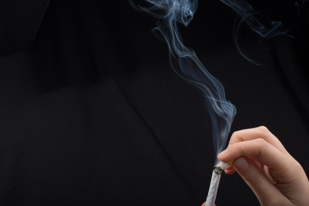 Hand is holding smoking cigarette with smoke aroundの写真素材