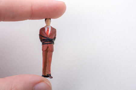 Hand holding tiny figurine of man model tied in a ropeの写真素材
