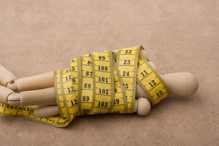 Yellow color measuring tape wrapped on wooden manの写真素材