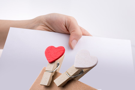 Hand holding a white sheet of paper with heart clips on itの写真素材