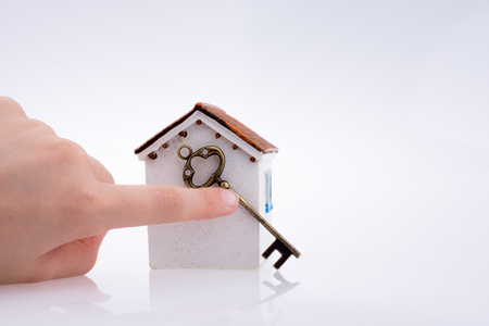 Hand holding a golden key near a house on a white backgroundの写真素材