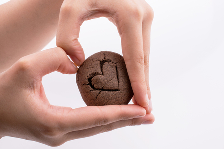 Hand holding a heart patterned chocolate cookie on a white backgroundの写真素材