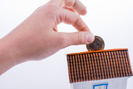 Hand dropping coin into the moneybox in the shape of a model houseの写真素材