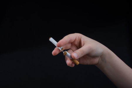 Hand is breaking a cigarette on a black backgroundの写真素材