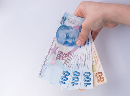 Hands holding American dollar banknotes and Turksh Lira banknotes side by side on white background